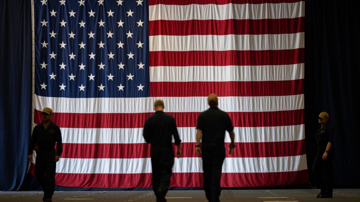 Navy soldiers walk in front of an American Flag