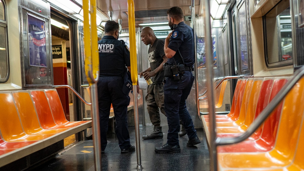  New York Police Department officers order a subway traveler to leave the car