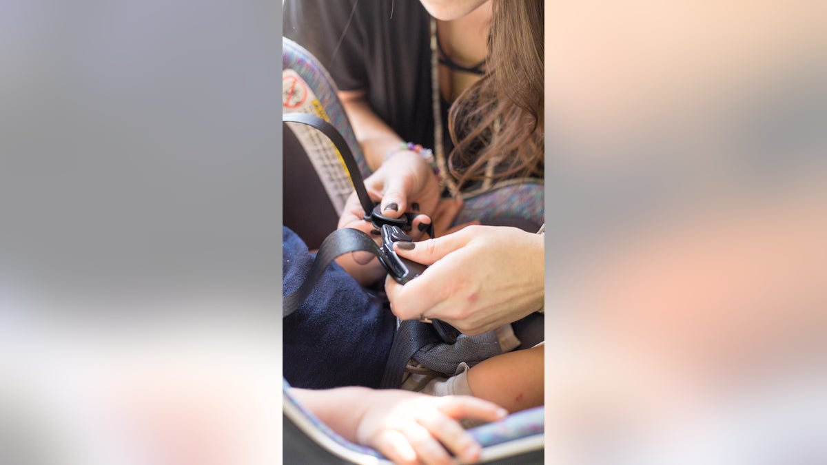 Mother straps child into car seat