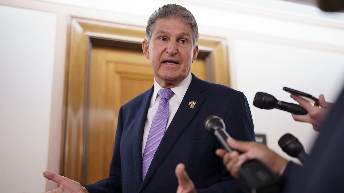 Sen. Joe Manchin wears dark suit and purple tie as he turns to speak into a reporter's mic