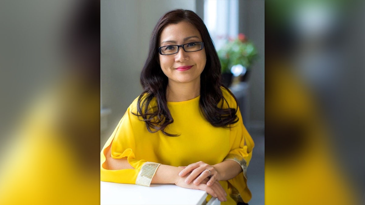 Shandra Woworuntu smiles at her desk in a yellow sweater