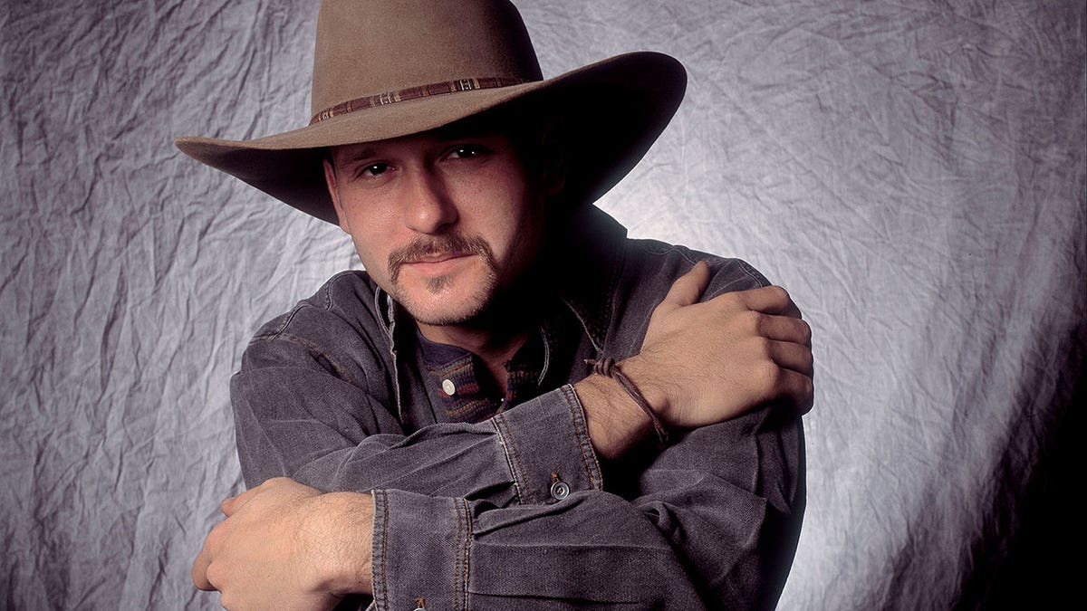 Tim McGraw poses in a cowboy hat and long-sleeve shirt