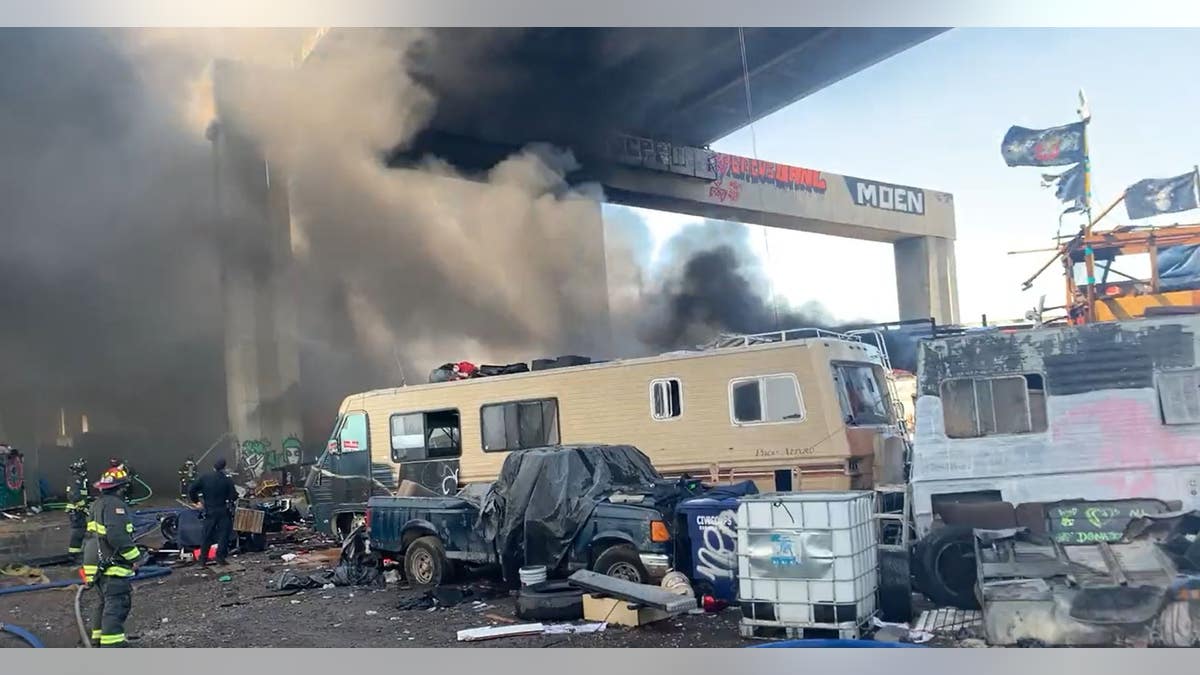 firefighters near an RV on fire with smoke under a bridge