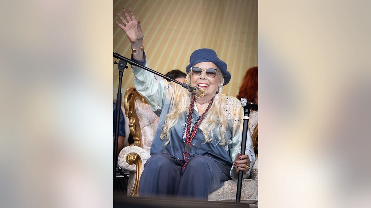 Joni Mitchell wearing a blue beret and sitting in a chair on stage
