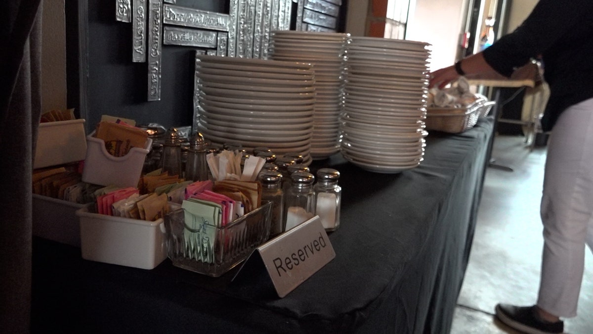A stack of plates sits next to sugar packets on a restaurant table with a "reserved" sign