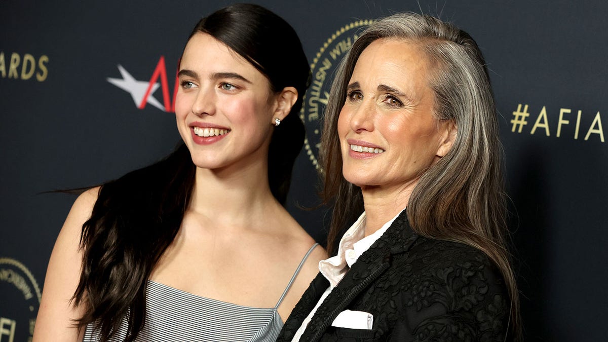 Margaret Qualley wears a grey dress on the red carpet with long dark hair next to mother Andie MacDowell in a dark suit