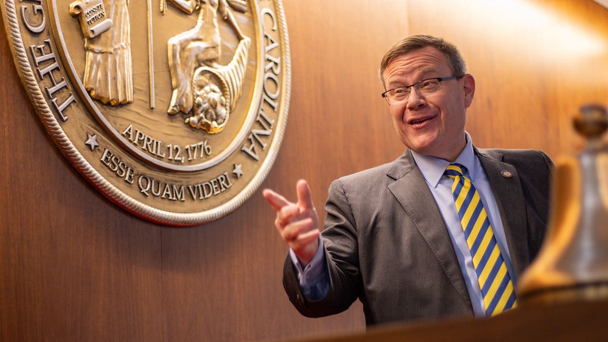 Rep Timothy Moore points while in front of state seal