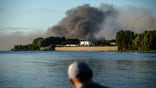 A fisherman watches smoke rise after Russian forces launched a missile attack on a military unit in the Vyshhorod district on the outskirts of Kyiv, Ukraine, Thursday, July 28, 2022.