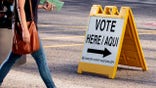 A resident walks past a "Vote Here" sign outside a polling location at the Burton Barr Central Library in Phoenix, Arizona, U.S., on Tuesday, Aug. 27, 2018. The Arizona primary is taking place just three days after the death of the state's senior senator, John McCain, a towering figure in U.S. politics for decades. Photographer: Caitlin O'Hara/Bloomberg via Getty Images