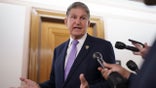 Sen. Joe Manchin wears dark suit and purple tie as he turns to speak into a reporter's mic