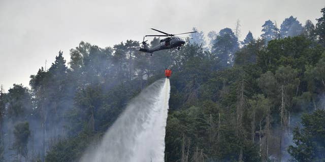 A helicopter drops water as a fire burns in the area of ​​the České Svycarsko National Park, Czech Switzerland, near Hrensko, Czech Republic.