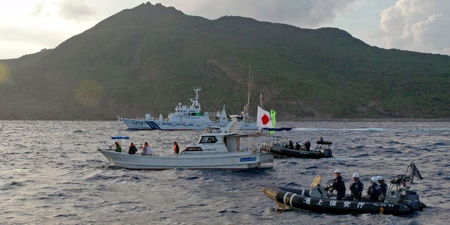 FILE: A Japanese Coast Guard vessel and boats, rear and right, sail alongside a Japanese activists' fishing boat, center with a flag, near a group of disputed islands called China's Diaoyu and Japan's Senkaku, early Sunday morning, Aug. 1. 18, 2013.