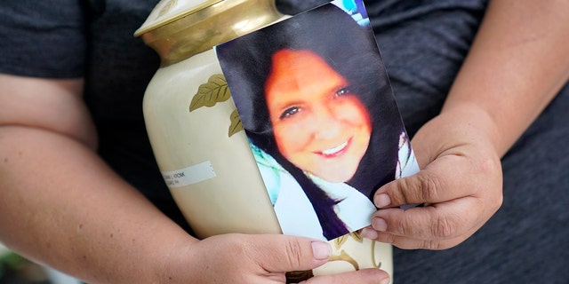 Kelly Titchenell sits on her porch in Mather, Pa., holding a photo of her mother Diania Kronk, and an urn containing her mother's ashes, Thursday, July 7, 2022.