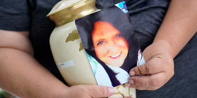 Kelly Titchenell sits on her porch in Mather, Pa., holding a photo of her mother Diania Kronk, and an urn containing her mother's ashes, Thursday, July 7, 2022.