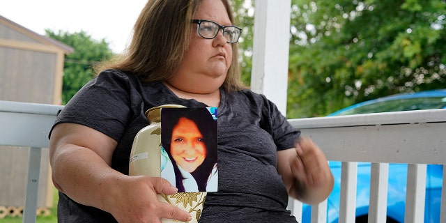 Kelly Titchenell sits on her porch in Mather, Pa., holding a photo of her mother Diania Kronk, and an urn containing her mother's ashes, Thursday, July 7, 2022.