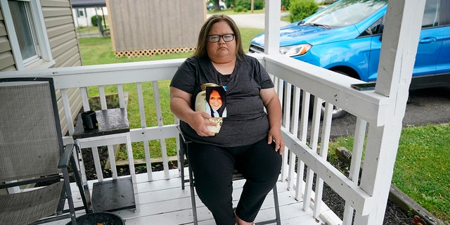 Kelly Titchenell sits on her porch in Mather, Pa., holding a photo of her mother Diania Kronk, and an urn containing her mother's ashes, Thursday, July 7, 2022. 