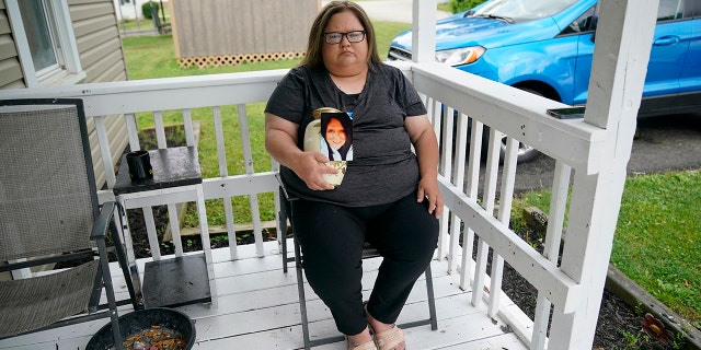 Kelly Titchenell sits on her porch in Mather, Pa., holding a photo of her mother Diania Kronk, and an urn containing her mother's ashes, Thursday, July 7, 2022.