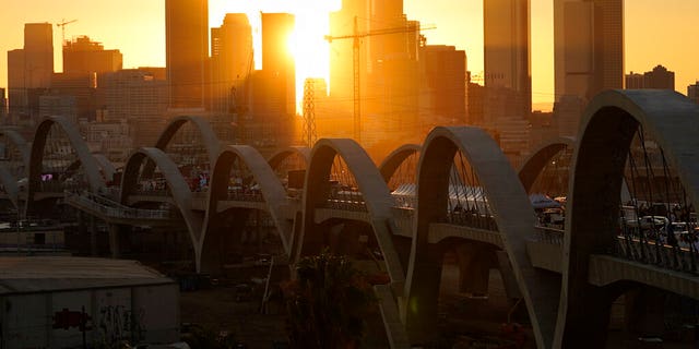 The sun sets behind the Los Angeles skyline during the opening ceremonies of the Sixth Street Bridge, a viaduct that connects the downtown Arts District with the historic Boyle Heights neighborhood. 