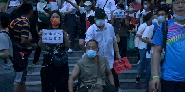 In this photo released by Yang on Sunday, July 10, 2022, people hold banners stage a protest at the branch of China's central bank in Zhengzhou in central China's Henan Province. The protesters assembled before dawn on Sunday in front of the People's Bank of China building in Zhengzhou. Police vehicles with flashing lights can be seen in videos taken in the early morning darkness. Police closed off the street and by 8 a.m. had started massing on the other side, Zhang said.