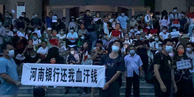 In this photo released by Yang on Sunday, July 10, 2022, people hold banners and chant slogans stage a protest at the entrance to a branch of China's central bank in Zhengzhou in central China's Henan Province. Hundreds of people held up banners and chanted slogans on the wide steps of the entrance to a branch of China's central bank in the city of Zhengzhou in Henan province, about 620 kilometers (380 miles) southwest of Beijing. Video taken by a protester shows plainclothes security teams being pelted with water bottles and other objects as they charge the crowd.