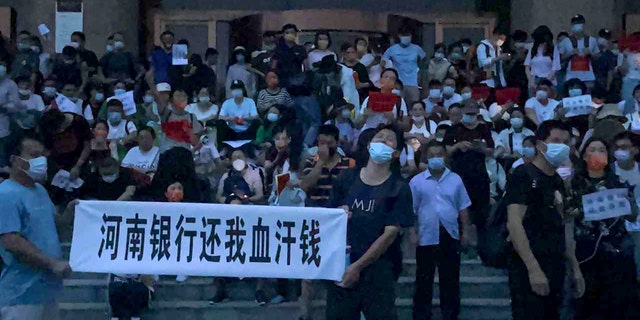 In this photo posted by Yang on Sunday, July 10, 2022, people hold banners and shout slogans, protesting at the entrance of a branch of the Chinese central bank in Zhengzhou in central China's Henan Province. About 620 kilometers (380 miles) southwest of Beijing, hundreds of people held banners and chanted on the broad steps of the entrance to a branch of the Chinese central bank in Zhengzhou city, Henan province. Video taken by a protester shows plainclothes security teams swarming with water bottles and other objects as they attack the crowd.