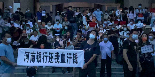 In this photo released by Yang on Sunday, July 10, 2022, people hold banners and chant slogans stage a protest at the entrance to a branch of China's central bank in Zhengzhou in central China's Henan Province. Hundreds of people held up banners and chanted slogans on the wide steps of the entrance to a branch of China's central bank in the city of Zhengzhou in Henan province, about 620 kilometers (380 miles) southwest of Beijing. Video taken by a protester shows plainclothes security teams being pelted with water bottles and other objects as they charge the crowd.