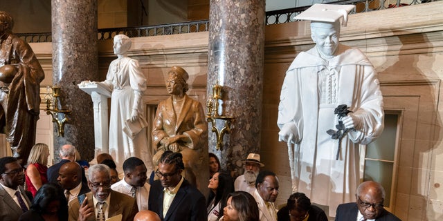 Evelyn Bethune, front left in yellow, a granddaughter of Mary McLeod Bethune watches as members of the Congressional Black Caucus gather around an unveiled statue of her grandmother, at a ceremony for the statue, which is the first state statue of a Black woman in Statuary Hall.