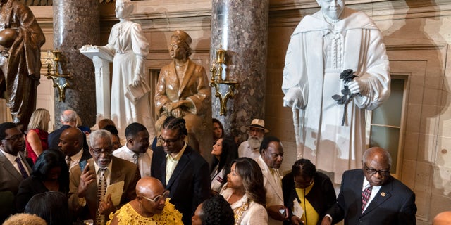 Evelyn Bethune, front left in yellow, a granddaughter of Mary McLeod Bethune watches as members of the Congressional Black Caucus gather around an unveiled statue of her grandmother, at a ceremony for the statue, which is the first state statue of a Black woman in Statuary Hall.