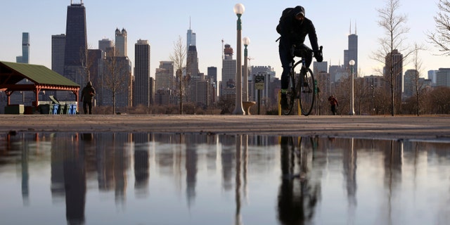 El horizonte de Chicago se refleja en el agua cuando un ciclista pasa por North Avenue Beach el 1 de marzo de 2021.