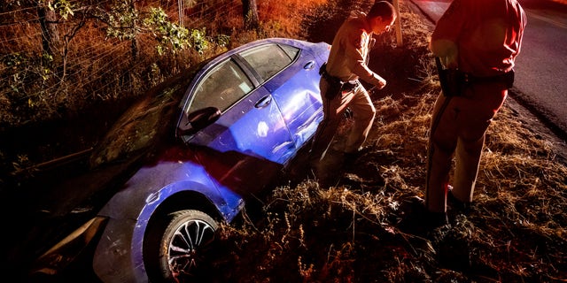 California Highway Patrol Officer Matthew Chance walks away from a car that crashed into a ditch while driving away from the Oak Fire in Mariposa County, Calif., on Friday, July 22, 2022.