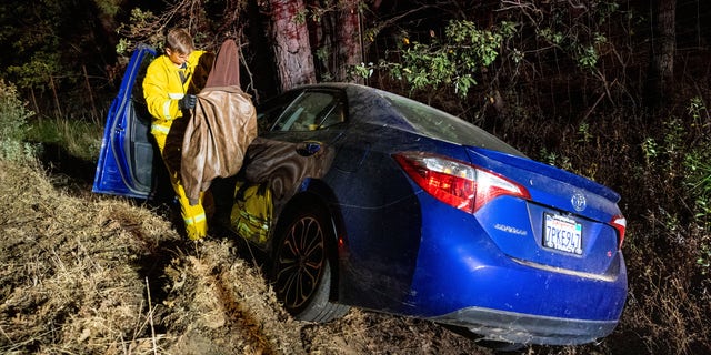 A firefighter removes a jacket from a car that crashed into a ditch while driving away from the Oak Fire in Mariposa County, Calif., on Friday, July 22, 2022. A police officer gave the elderly driver a ride out of the fire evacuation zone. 