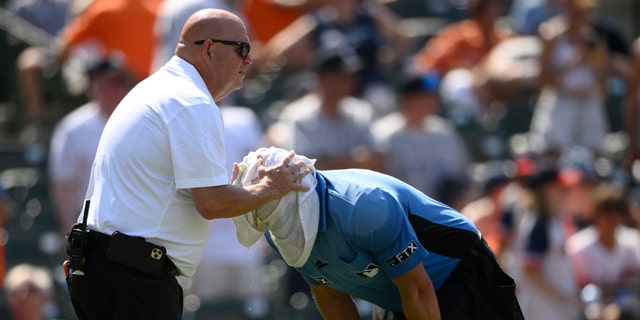 Baltimore Orioles head trainer Brian Ebel left, helps home plate umpire Scott Barry get relief from the heat with a wet towel around his head after the sixth inning of a baseball game between the Orioles and the New York Yankees in Baltimore.