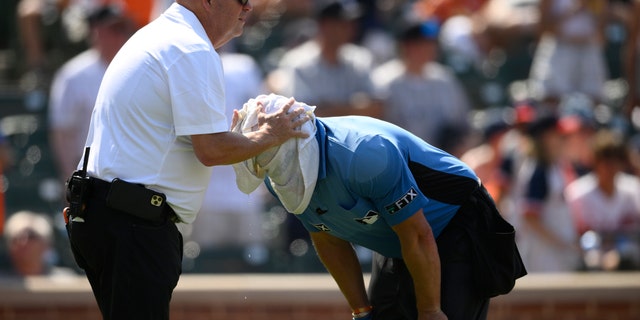 Baltimore Orioles head trainer Brian Ebel left, helps home plate umpire Scott Barry get relief from the heat with a wet towel around his head after the sixth inning of a baseball game between the Orioles and the New York Yankees in Baltimore.