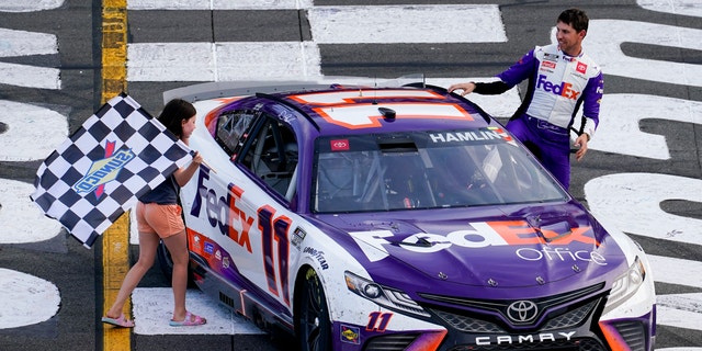 Taylor James Hamlin, left, carries the checkered flag with her dad, Denny Hamlin, after he won a NASCAR Cup Series auto race at Pocono Raceway, in Long Pond, Pa. NASCAR stripped Hamlin of his win when his No. 11 Toyota failed inspection and was disqualified, awarding Chase Elliott the Cup Series victory. 