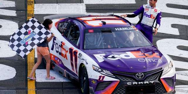 Taylor James Hamlin, left, carries the checkered flag with her dad, Denny Hamlin, after he won a NASCAR Cup Series auto race at Pocono Raceway, in Long Pond, Pa. NASCAR stripped Hamlin of his win when his No. 11 Toyota failed inspection and was disqualified, awarding Chase Elliott the Cup Series victory.