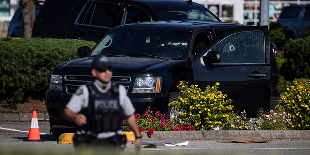 A police officer standing near a windshield and passenger window of an RCMP vehicle with bullet holes at the scene of a shooting in Langley, British Columbia, Monday, July 25, 2022. 