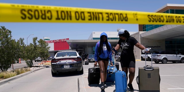 Passengers walk in a parking area outside Dallas Love Field Airport on Monday, July 25, 2022, after a woman opened fire, apparently on the roof. 