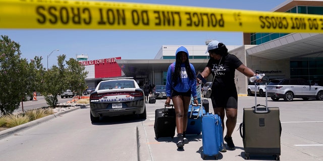 Travelers walk to a parking area outside of Dallas Love Field Airport, Monday, July 25, 2022, after a woman fired several gunshots, apparently at the ceiling. 