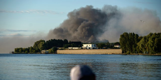 A fisherman observes the rise in smoke after Russian forces launched a missile attack on a military unit in the Vyshhorod district on the outskirts of Kiev, Ukraine on Thursday, July 28, 2022. 