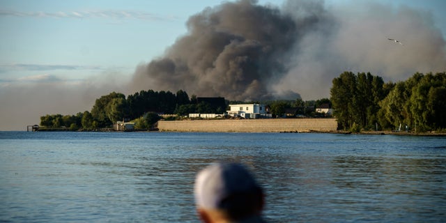 A fisherman observes the rise in smoke after Russian forces launched a missile attack on a military unit in the Vyshhorod district on the outskirts of Kiev, Ukraine on Thursday, July 28, 2022. 