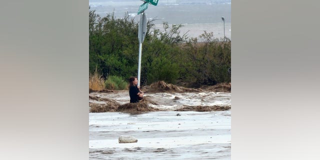 The 42-year-old woman was spotted hanging on to a stop sign as waist-deep water swirled around her.