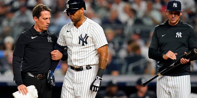 New York Yankees manager Aaron Boone, right, waits as a trainer checks on Aaron Hicks, who was hurt during an at-bat during the third inning of the team's baseball game against the Cincinnati Reds on Tuesday, July 12, 2022, in New York.