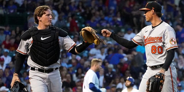 Baltimore Orioles catcher Adley Rutschman, left, acknowledges starting pitcher Spenser Watkins' strikeout of Chicago Cubs' Ian Happ, center, to end the third inning of a baseball game Wednesday, July 13, 2022, in Chicago. 