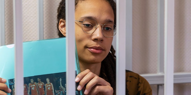 WNBA star and two-time Olympic gold medalist Brittney Griner holds up a photo of players from the recent all star game wearing her number, sitting in a cage in a courtroom ahead of a hearing in the Khimki district court, just outside Moscow, Russia , Friday, July 15, 2022. 