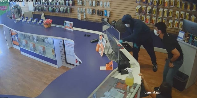 Armed gunman robbed a Boost Mobile store near Los Angeles over the weekend. He is seen here going through a cash register in front of two store employees.