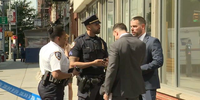 An NYPD officer speaks with a group outside the Upper East Side Chase bank where a security guard was stabbed Friday morning.