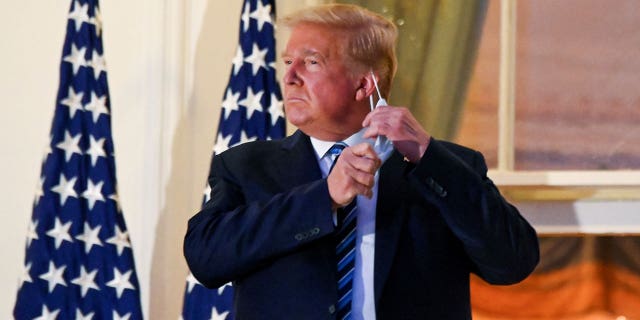 U.S. President Donald Trump pulls off his protective face mask as he poses atop the Truman Balcony of the White House after returning from being hospitalized at Walter Reed Medical Center for COVID-19 treatment, in Washington on October 5, 2020.