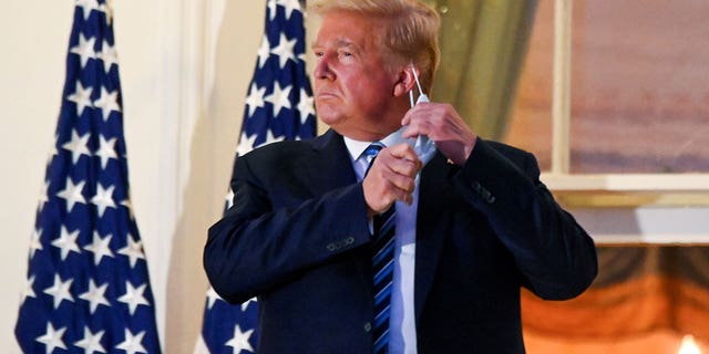 U.S. President Donald Trump pulls off his protective face mask as he poses atop the Truman Balcony of the White House after returning from being hospitalized at Walter Reed Medical Center for COVID-19 treatment, in Washington on October 5, 2020.