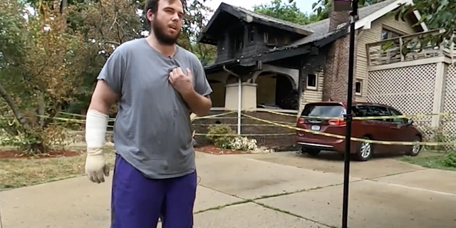 Nick Bostic stand in front of a home that caught fire Monday. Bostic rushed into the burning house and was able to help get four children and an adult to safety.