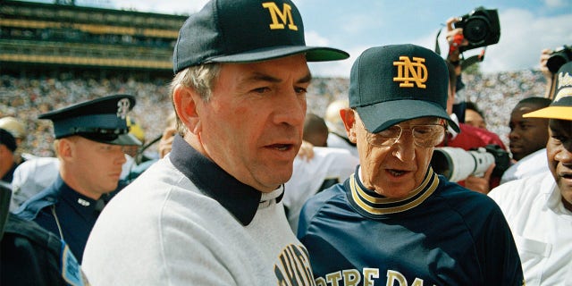 Notre Dame coach Lou Holtz (right) is congratulated by Michigan coach Gray Moeller (left) after Notre Dame's victory over Michigan on September 11, 1993 in Ann Arbor, Michigan. Former Michigan, Illinois, and Detroit coach Lions Meller died on Monday, July 11, 2022. He was 81 years old. The University of Michigan announced his death and no cause was given.
